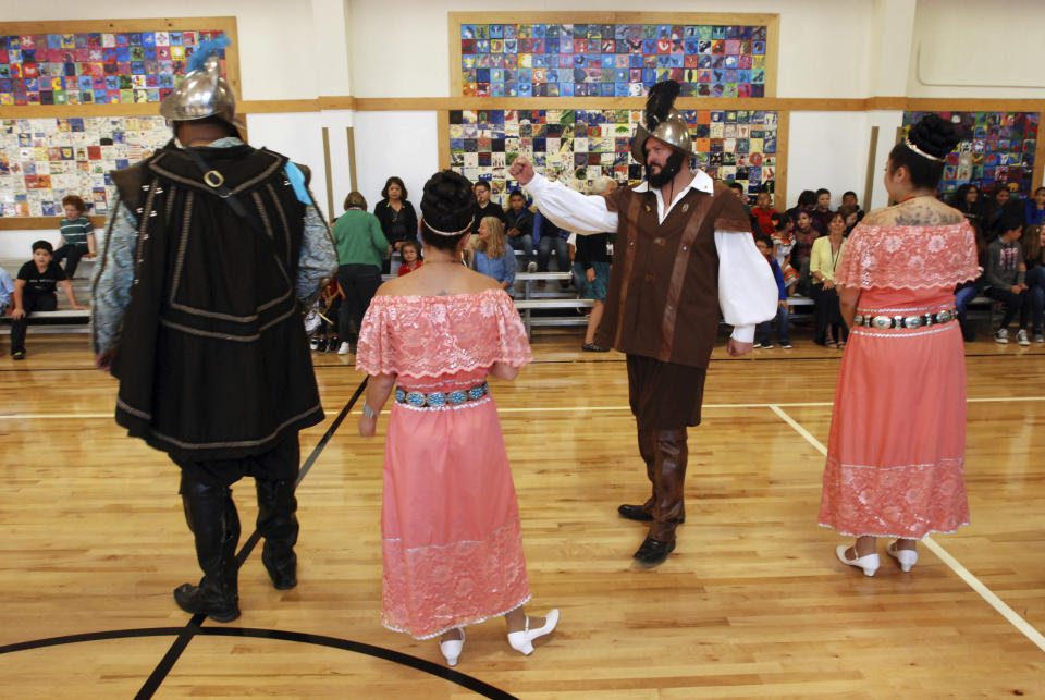 In this Aug. 30, 2017, file photo, Edwin Quintana, second from right, dressed as a 17th Century Spanish, conquistador motions to a crowd of students at Tesuque Elementary school in Tesuque, N.M., during an annual presentation of Spanish colonial culture and history that honors conquistador Don Diego de Vargas. In recent years, the conquistador and all the effigies connected to it have come under intense criticism from Native American activists who say the image glorifies indigenous genocide and needs to be removed from schools, streets and seals. (AP Photo/Morgan Lee)