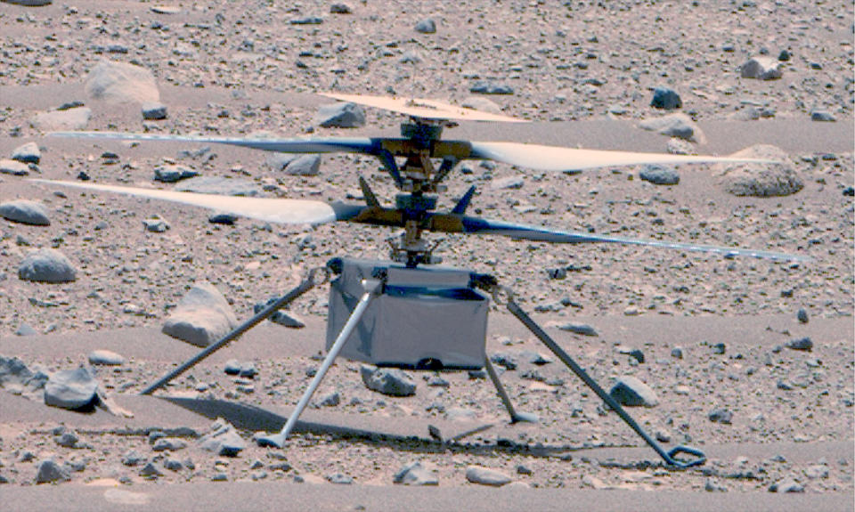 A close-up view of a small, quad-rotor drone resting on the surface of Mars.