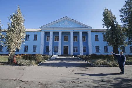 An exterior view shows a building, damaged after a firing attack, which is expected to serve as a polling station, with a member of a local electoral commission seen in the foreground, in Yasynuvata (Yasinovataya) in Donetsk region, eastern Ukraine October 30, 2014. REUTERS/Maxim Zmeyev