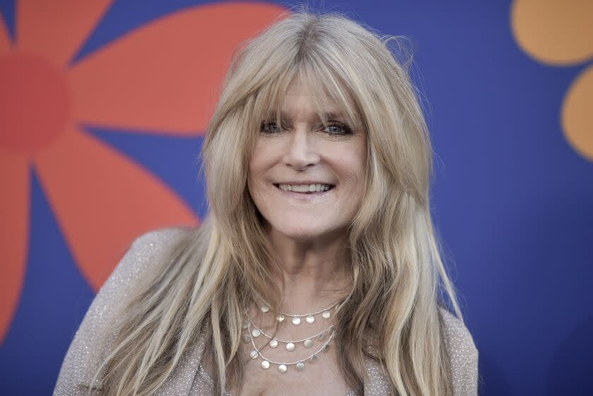 Susan Olsen smiles in a beige outfit and silver jewelry.