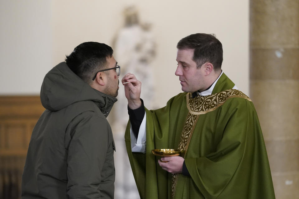 Father Matthew Hood distributes Holy Communion at Our Lady of the Rosary church Friday, Feb. 18, 2022, in Detroit. In 2020, one word caught the ear of a young Detroit-area Catholic priest while he watched a video of his baptism from decades earlier. "Wait," the Rev. Matthew Hood recalled thinking. "Something doesn't seem right here." Indeed, an error by a deacon had spoiled the sacrament — and, in domino-like fashion, meant he truly wasn't a priest. (AP Photo/Paul Sancya)