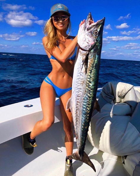 A photo of the 'World's sexiest extreme fisher' Emily Reimer wearing a blue bikini on a boat holding a fish.