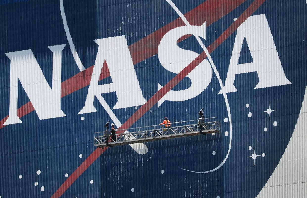 Workers freshen up the paint on the NASA logo on the Vehicle Assembly Building before the arrival of NASA astronauts Bob Behnken and Doug Hurley at the Kennedy Space Center on May 20, 2020 in Cape Canaveral, Florida: Joe Raedle/Getty Images