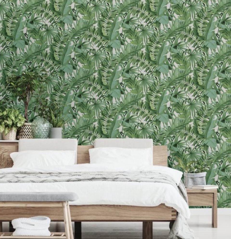 A bedroom decorated with wallpaper with green leaves all over it