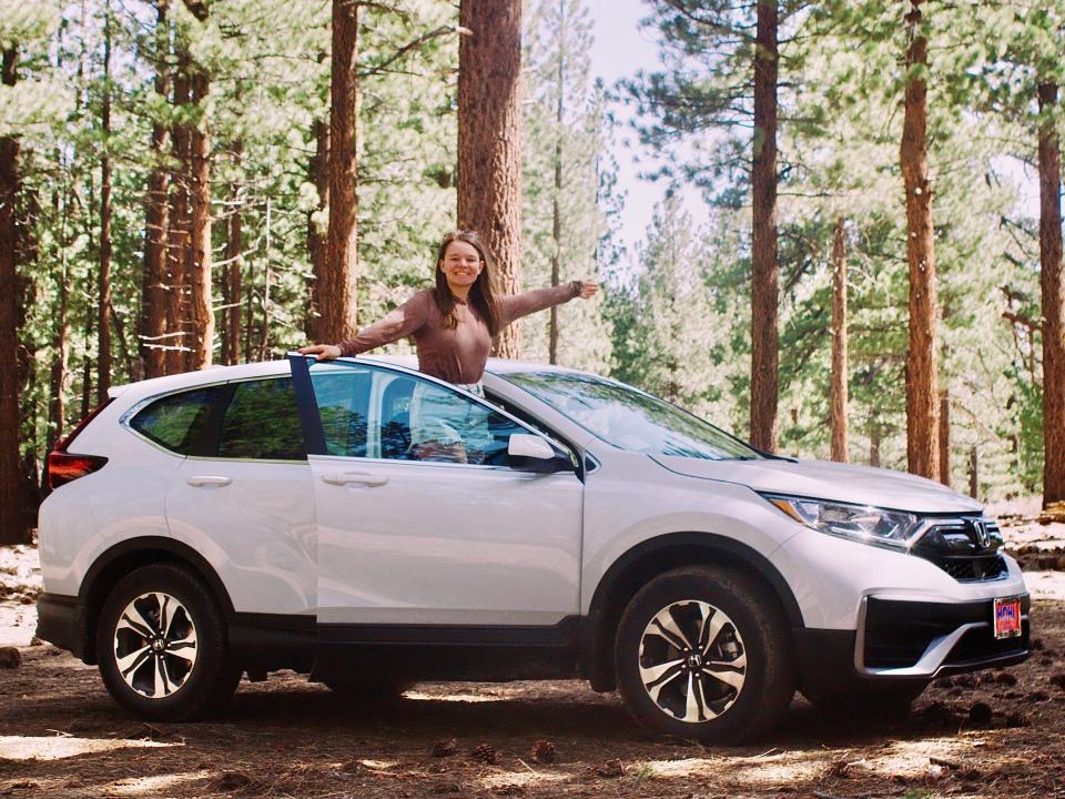 Nicole standing in her white subaru in the middle of the forest