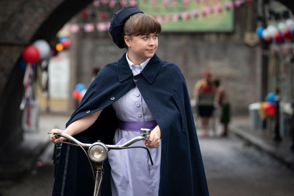 call the midwife nancy corrigan in her uniform walking with her bicycle