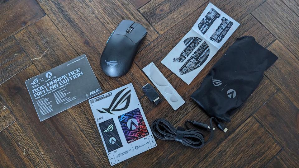 The accessories of the ASUS ROG Harpe; manual, stickers, mouse feet, grip tape, cable, wireless receiver and a wireless dongle.