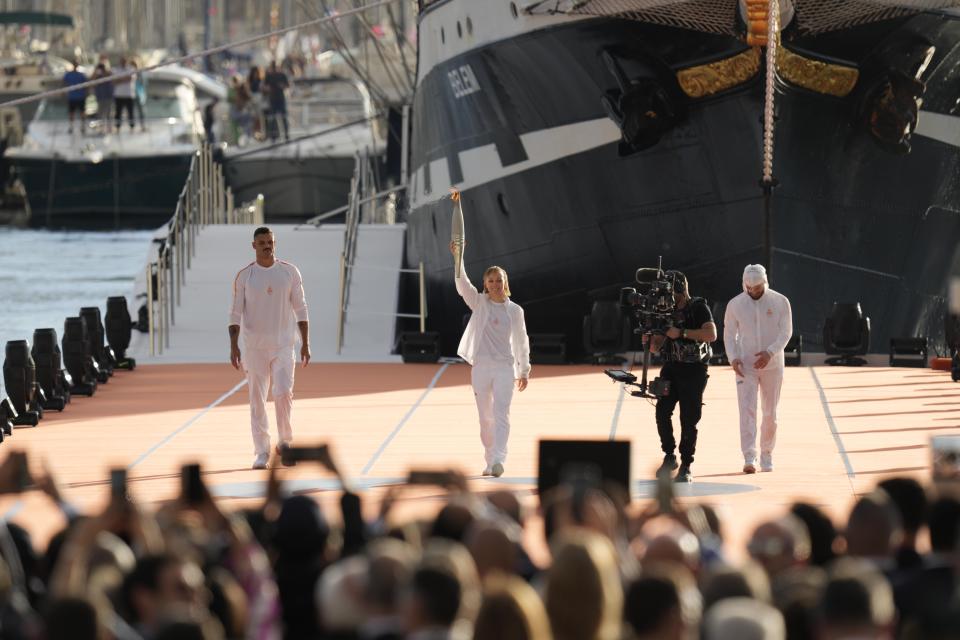 French Paralympic athlete Nantenin Keïta, holds the Olympic flanked by first torch carrier in France French Olympic swimmer Florent Manaudou, left , and French rap artist Jul during the torch arrival ceremony in Marseille, southern France. After leaving Marseille, a vast relay route is undertaken before the torch odyssey ends on July 27 in Paris. The Paris 2024 Olympic Games will run from July 26 to Aug.11, 2024. (AP Photo/Thibault Camus)