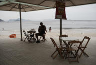A man sits at an empty restaurant that is open for business on Copacabana beach in Rio de Janeiro, Brazil, Friday, March 20, 2020. Amid the worldwide spread of the new coronavirus, no lockdowns have been ordered and state governments and municipalities have taken the lead in telling people to stay home. (AP Photo/Silvia Izquierdo)