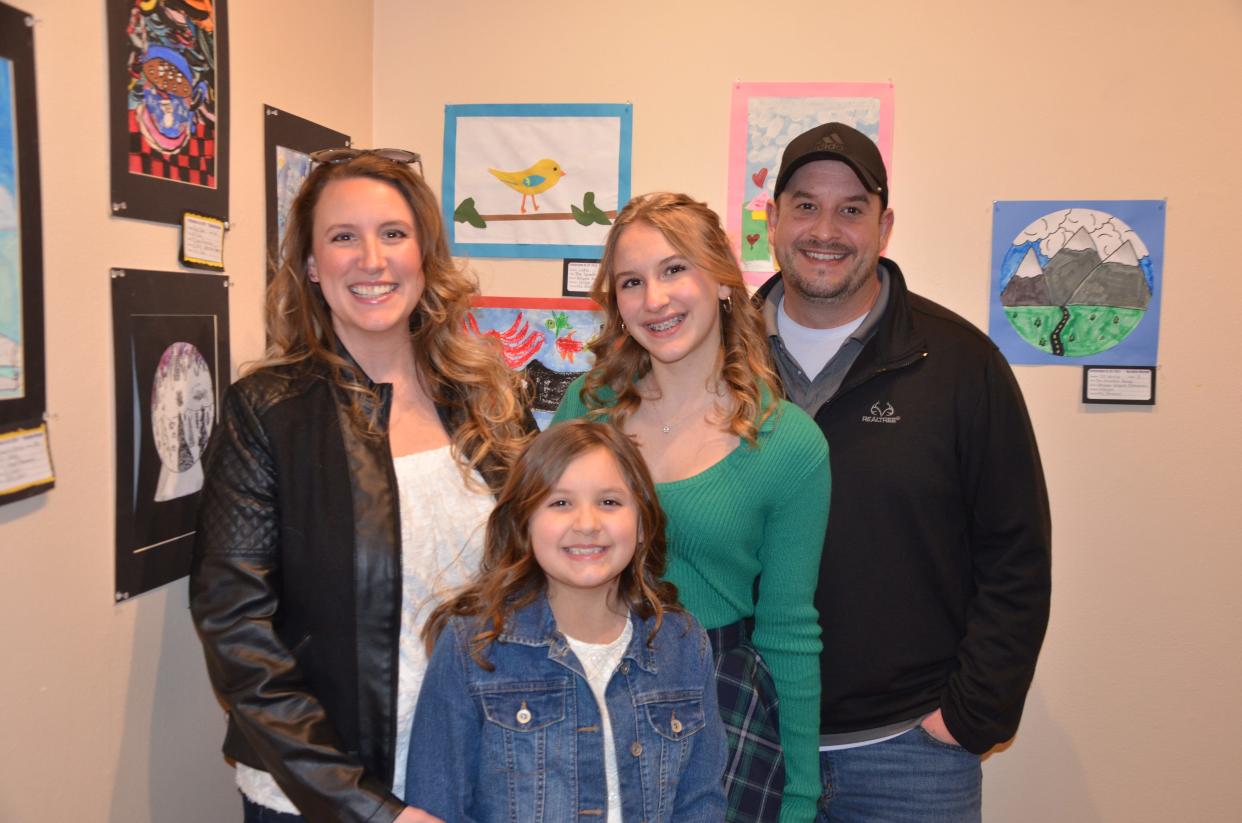 Lydia, a third-grader at Whipple Heights Elementary School, poses with her family in front of her collage, "The Colorful Bird," at the exhibition opening.