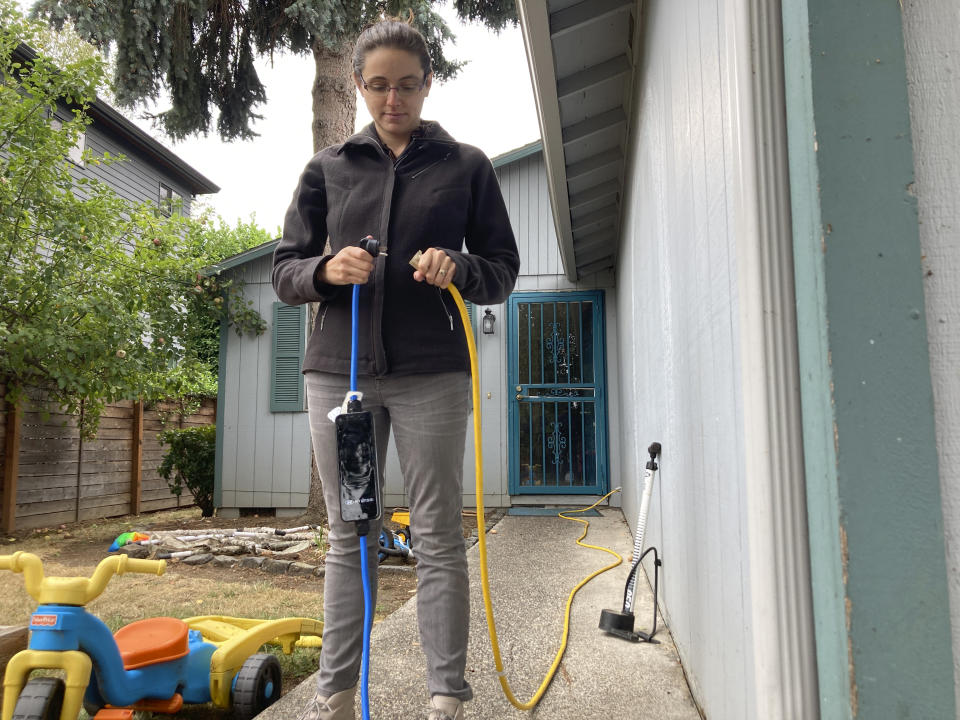 Rebecca DeWhitt shows how she connects an extension cord to her electric vehicle's charging cable outside the Portland, Ore., home she rents on Sept. 30, 2022. DeWhitt and her partner aren't allowed to use the rental home's garage and so they charge their EV using an extension cord that plugs into a standard electrical outlet outside their front door. The great transition to electric vehicles is underway but for millions of renters like DeWhitt, access to charging remains a significant barrier. (AP Photo/Gillian Flaccus)