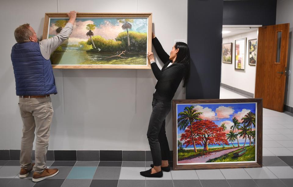 Sarasota art collector Allan Asselstine, left, and Pui Lightle from Highwaymen Art Specialists, hang a painting by Albert Hair, one of the original Florida Highwaymen. A painting of a royal poinciana tree by James Gibson, behind Lightle will also be part of the exhibit.
