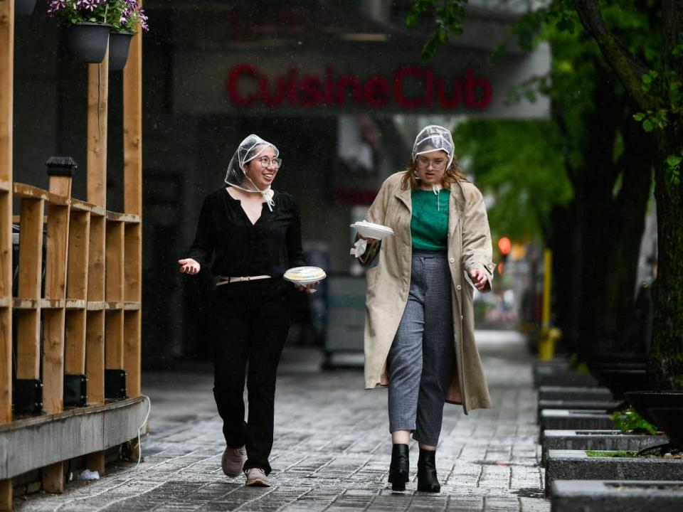 Courtney Shields, left, and Hannah Duhme wear the rain bonnets they purchased at a nearby pharmacy after discovering umbrellas were sold out during rainfall in Ottawa on May 17, 2022. (Justin Tang/The Canadian Press - image credit)