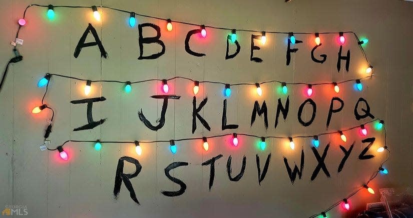 a photo from a real estate listing showing a wall with the alphabet written on it in black paint and string lights between