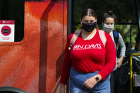 FILE - Masked students disembark from a bus on the campus of Ball State University in Muncie, Ind., Thursday, Sept. 10, 2020. Colleges across the country are struggling to salvage the fall semester as campus coronavirus cases skyrocket and tensions with local health leaders flare. Schools have locked down dorms, imposed mask mandates, barred student fans from football games and toggled between online and in-person classes. (AP Photo/Michael Conroy)