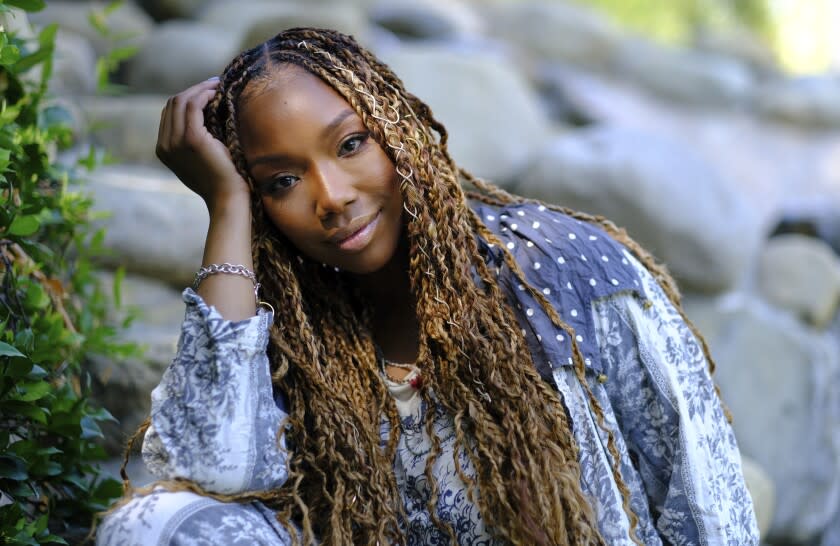 A woman with long, braided hair posing with a hand to her head