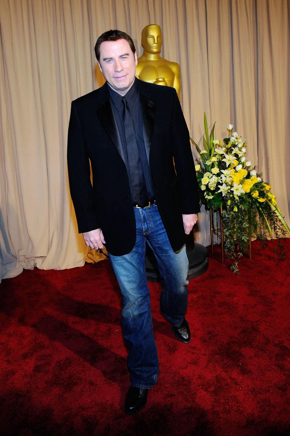 John in a black blazer, black button down and tie, and blue jeans.