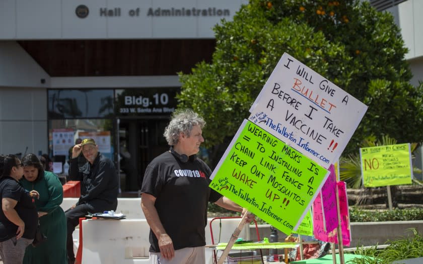 SANTA ANA, CA - JULY 14: Ron Miller, of La Habra, holds signs against he continued use of masks and the approval continuance of a local health emergency outside where the Orange County Board of Supervisors was holding its regular board meeting at the Orange County Hall of Administration on Tuesday, July 14, 2020 in Santa Ana, CA. OC Supervisors also discussed a file status report and approve continuance of local health emergency and local emergency related to Novel Coronavirus (COVID-19) and set a review to continuing local emergency and every 30 days after until terminated. They also discussed a resolution in support of a ban on affirmative action introduced by Supervisors Michelle Steel and Don Wagner and a proposal from Supervisors Lisa Bartlett and Doug Chaffee to alter the county's term limits for supervisors. (Allen J. Schaben / Los Angeles Times)