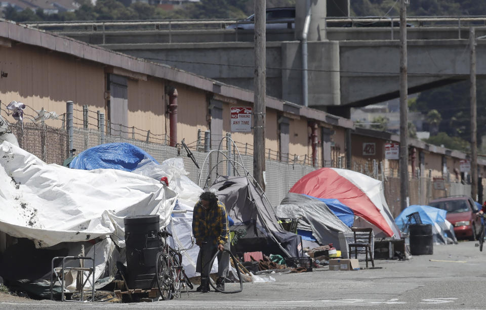 FILE - This Thursday, June 27, 2019, photo shows a man holding a bicycle tire outside of a tent along a street in San Francisco. San Franciscans should put aside their political differences and support finding homes for more than 1,000 homeless people, according to a public engagement campaign beginning Thursday, July 25, 2019. (AP Photo/Jeff Chiu, File)