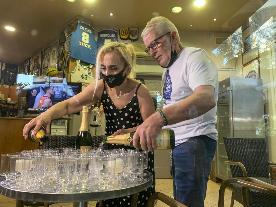 Coffee shop owner Yiannis Tzikas and his wife Kaiti Drimba pour champagne into plastic glasses after the Milwaukee Bucks win the NBA title, in the Sepolia district of Athens on Wednesday, July 21, 2021. Milwaukee Bucks star Giannis Antetokounmpo grew up in Sepolia and used to stop at the coffee shop before basketball practice as a teenager. (AP Photo/Derek Gatopoulos)