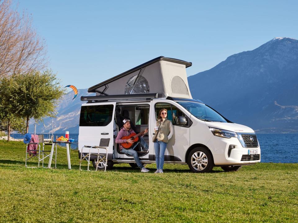 The Nissan Seaside by Dethleff camper van parked as two people hang out around the van. The roof is popped.