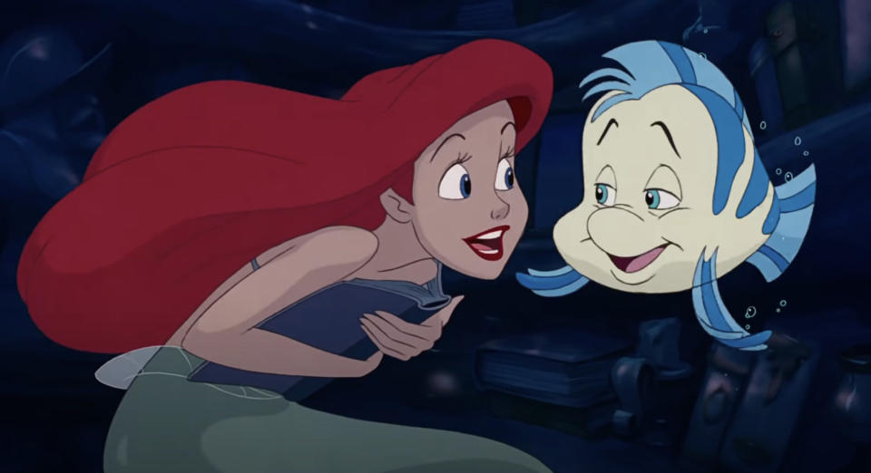 Ariel holding a book and talking to Flounder