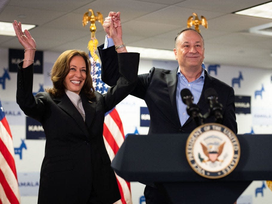 Kamala Harris and Doug Emhoff hold hands and smile at the Harris campaign headquarters.