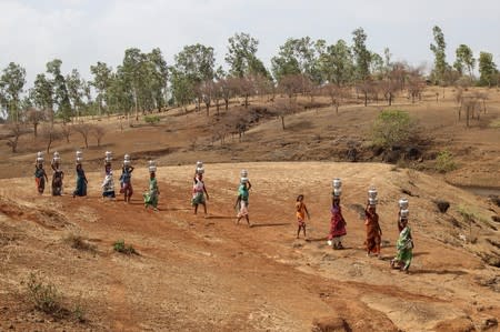 Women carry pitchers filled with water from an opening made to filter water next to a polluted lake in Thane