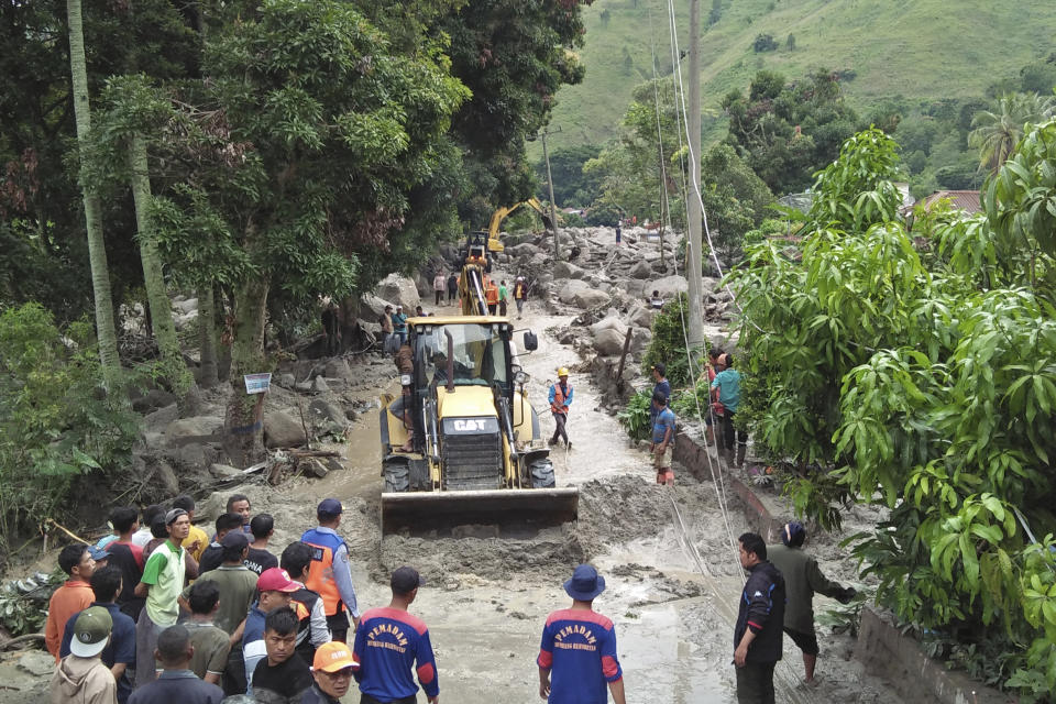 Rescue workers use heavy machines to clear a road from rock and mud following a landslide in Simangulampe village, North Sumatra, Indonesia, Saturday, Dec. 2, 2023. Torrential rain triggered flash floods and a landslide on Indonesia's Sumatra island, leaving a number of people missing, officials said Saturday. (AP Photo/Hermanto Tobing)
