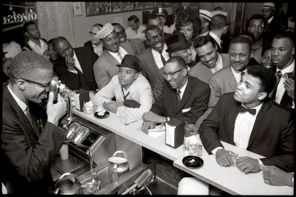 Malcolm X enfoca con su cámara a Cassius Clay, sentado en el mostrador de la Hampton House de Miami en 1964, rodeado de admiradores después de que venciera a Sonny Liston por el campeonato mundial de los pesos pesados, el 25 de febrero de 1964, en Miami Beach. Al día siguiente, Clay anunció que se había hecho miembro de la Nación del Islam y cambió su nombre por el de Muhammad Ali.