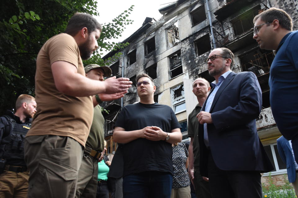 In this photo provided by the Ukrainian Foreign Ministry Press Office, Austrian Foreign Minister Alexander Schallenberg, second right, and Czech Republic's Foreign Minister Jan Lipavsky, center, talk with local authorities against the background of the houses destroyed by the Russian shelling in Hostomel, close to Kyiv, Ukraine, Wednesday, July 20, 2022. (Ukrainian Foreign Ministry Press Office via AP)