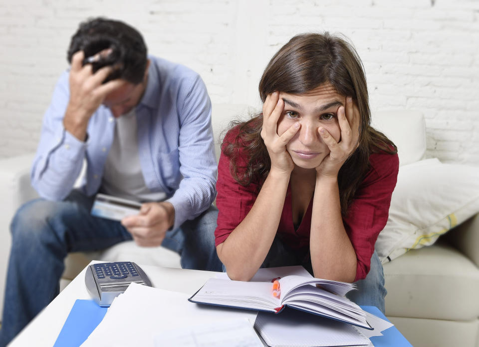 young couple stress sitting on living room couch looking at a bill