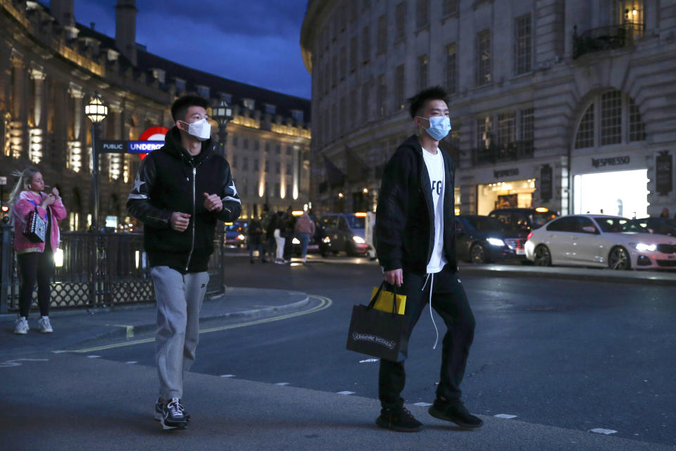 Two pedestrians cross the street wearing masks in Piccadilly Circus, London, Saturday, March 14, 2020. British Prime Minister Boris Johnson has described the worldwide pandemic as “the worst public health crisis for a generation.” (Hollie Adams/PA via AP)