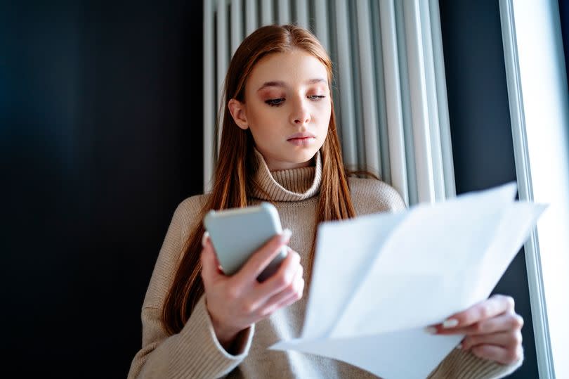 Woman looking at energy bill standing by radiator