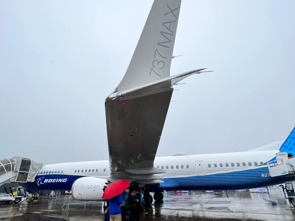 A Boeing 737 Max 10 at the Paris Air Show, with people sheltering from the rain underneath the wing, and the winglet with 737 MAX logo in the foreground