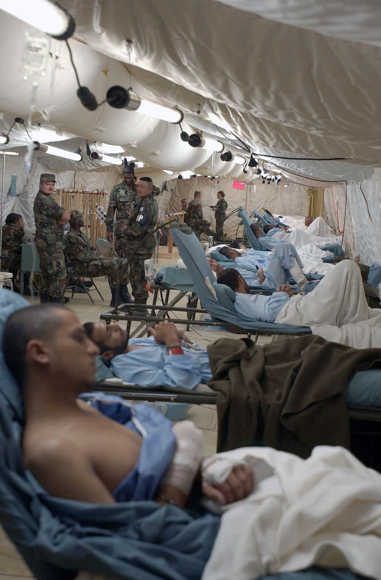 En una imagen publicada por el Departamento de Defensa, prisioneros extranjeros, presuntamente cautivos en el campo de batalla, son tratados dentro de una tienda médica en la Base Naval de Guantánamo en Cuba, que para entonces albergaba a 158 detenidos, el 20 de febrero de 2002. Para entonces, el personal médico tenía muletas y equipos de fisioterapia en el lugar; cada detenido tenía grilletes en las muñecas y los tobillos. En la tienda había miembros de la Marina, el Ejército y los Marines.