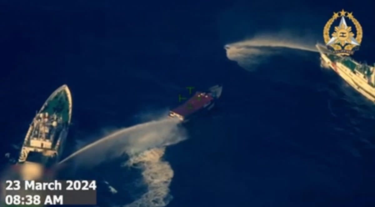 This frame grab from handout aerial video footage taken and released on 23 March 2024 by Philippines Armed Forces shows China Coast Guard ships (L and R) deploying water cannon against the Philippine military-chartered civilian boat Unaizah (ARMED FORCES OF THE PHILIPPINES/)