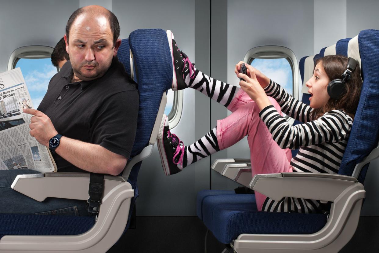 A carefree young girl annoying the passenger infront by pushing his seat.