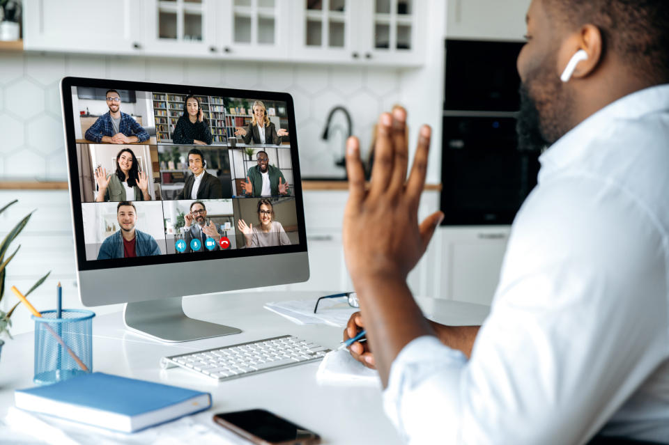 Person waves at colleagues during a virtual meeting displayed on a computer screen