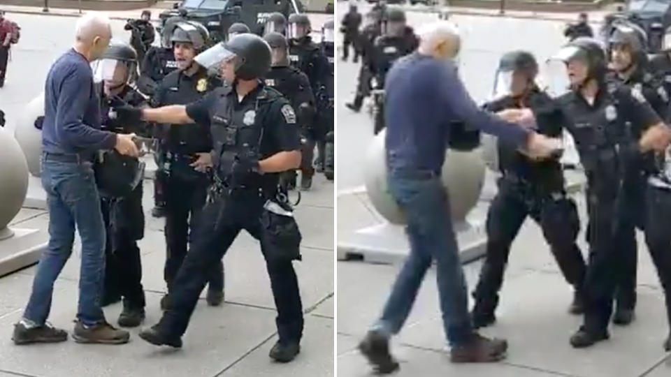 An elderly man walks up to police in full riot gear, two police officers push the man back and he falls backward hitting his head on the concrete. 