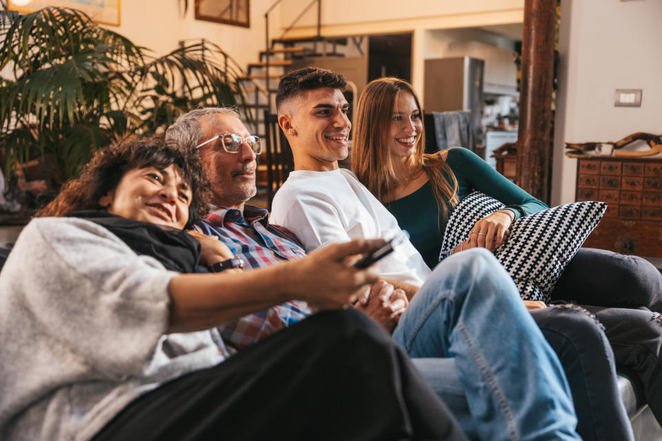 Family, father, mother and sons sitting on the living room’s sofa and watching TV together.