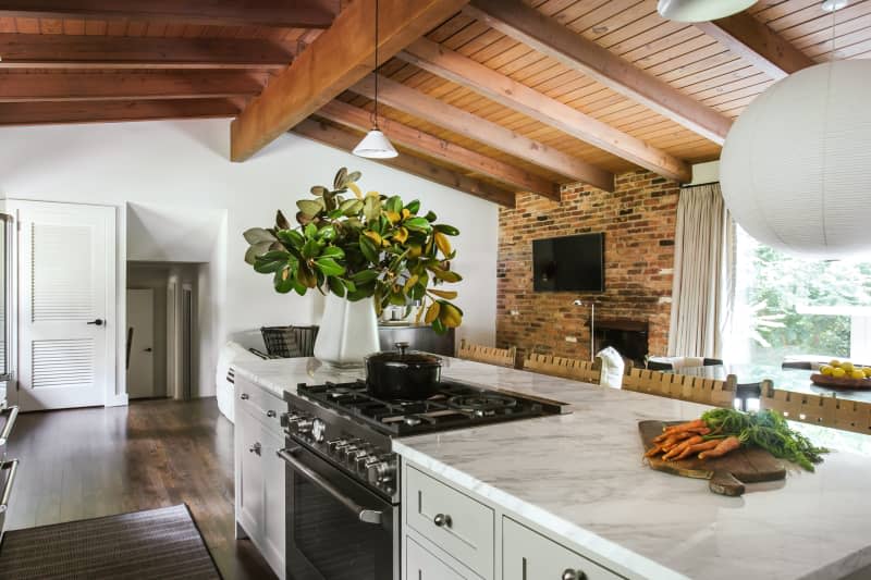 red wood ceiling, large wood beams, kitchen island with white marble, open floor plan, brick walled fireplace