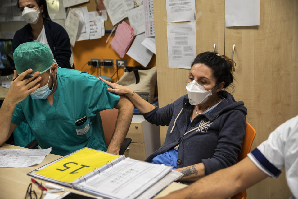 In this photo taken on Friday, April 10, 2020 nurse Cristina Settembrese places her hand on a colleagues shoulder during the night meeting at the end of her work shift in the COVID-19 ward at the San Paolo hospital in Milan, Italy. (AP Photo/Luca Bruno)
