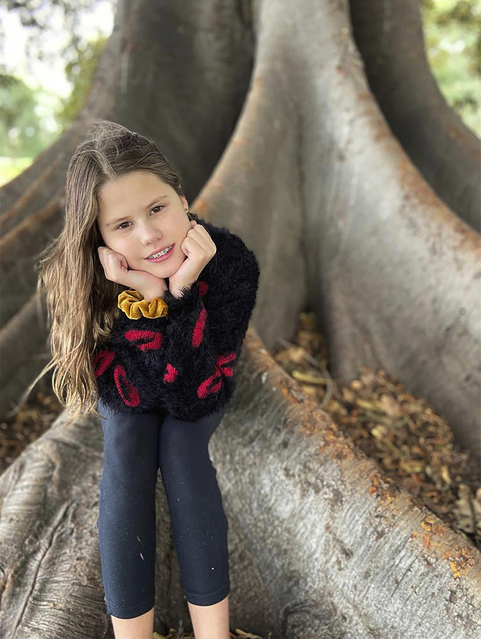 In this photo provided by her family, Niki Jolene Berghamre-Davis, 11, sits on the roots of a gum tree in Port Melbourne, Australia, on April 30, 2020. While sad about all the people lost to the virus pandemic, Niki is hopeful that the shutdowns are teaching the world how to live in ways that will help the environment. (Anna Berghamre via AP)