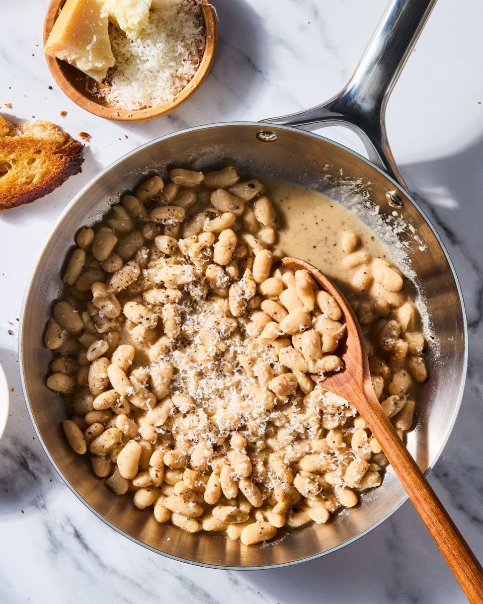 cacio e pepe white beans skillet with a wooden spoon and a bowl of parmesan cheese