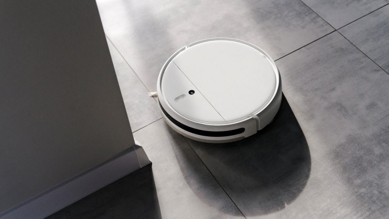  A white robot vacuum on a grey tiled floor 