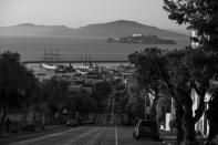 Cars are parked along an empty Hyde Street looking down toward the historic ships at Hyde Street pier and Alcatraz Island in San Francisco on May 7, 2020. Normally, the months leading into summer bring bustling crowds to the city's famous landmarks, but this year, because of the coronavirus threat they sit empty and quiet. Some parts are like eerie ghost towns or stark scenes from a science fiction movie. (AP Photo/Eric Risberg)