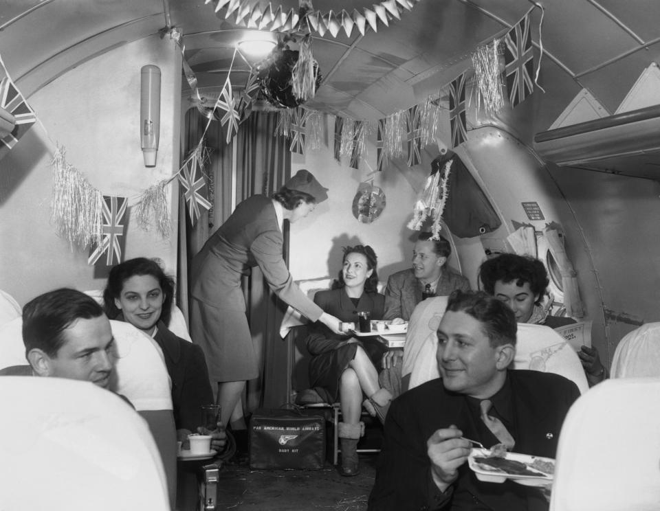 Air hostess Patricia Pelley serves an in-flight meal to passengers traveling across the Atlantic on board a festively decorated Pan American airplane.