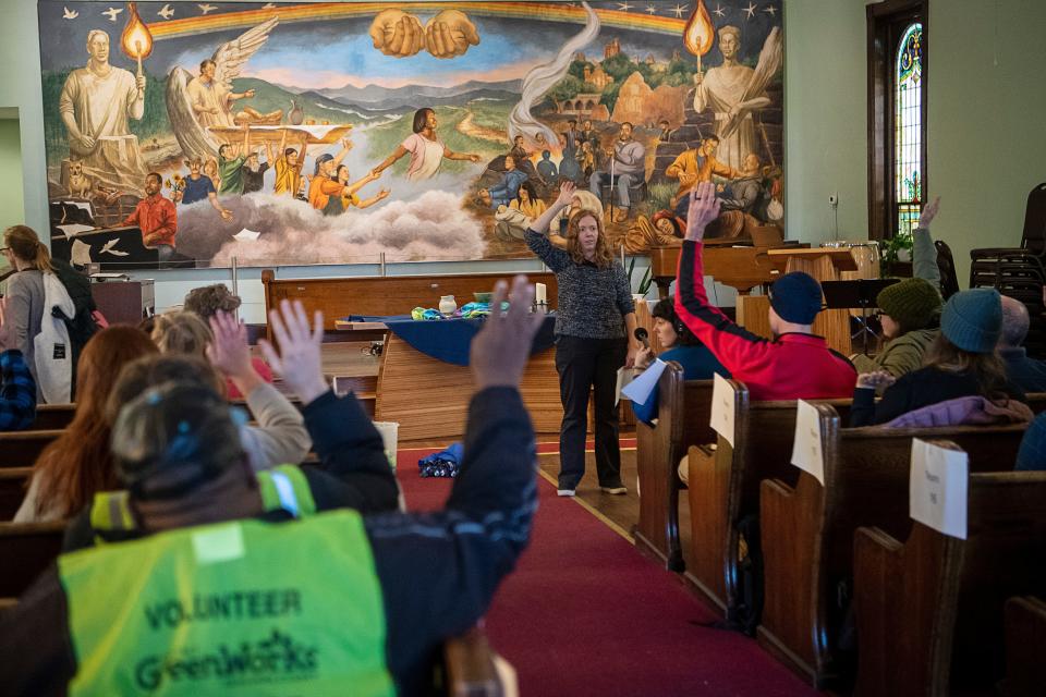 Volunteers raise their hands to indicate their previous participation in a point in time count as Debbie Alford, of Asheville city's Homeless Strategy Division, briefs them before the annual count of unhoused individuals, January 30, 2024, at Haywood Street Congregation.