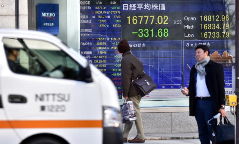 Pedestrians stand before a share prices board in Tokyo on January 16, 2015